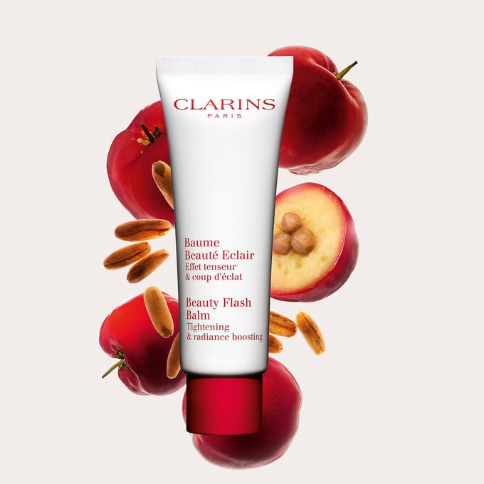 Packshot di un tubetto di Baume Beaut&eacute; Eclair Clarins vicino a bacche di acerola su uno sfondo color pesca.