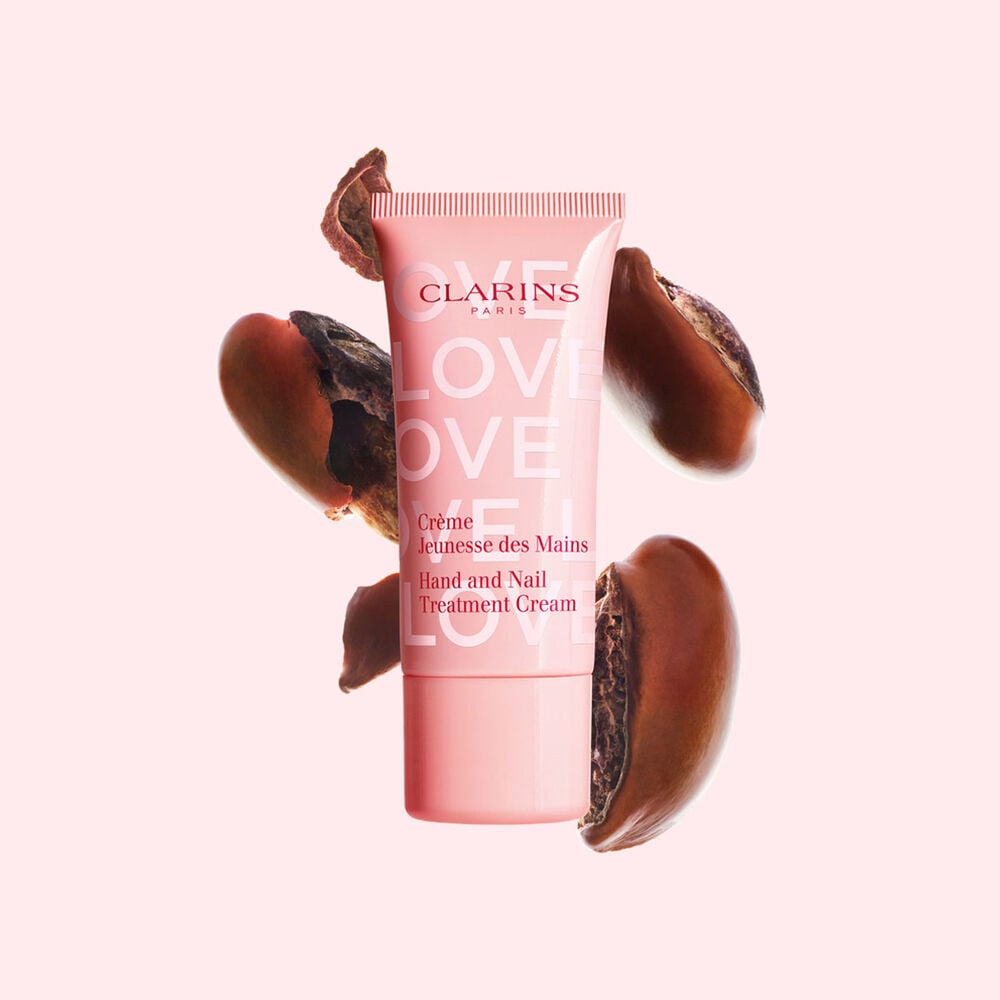 Packshot della crema mani della collezione Love in edizione limitata davanti a semi di karit&eacute; su uno sfondo rosa chiaro che enfatizza l&rsquo;ingrediente chiave