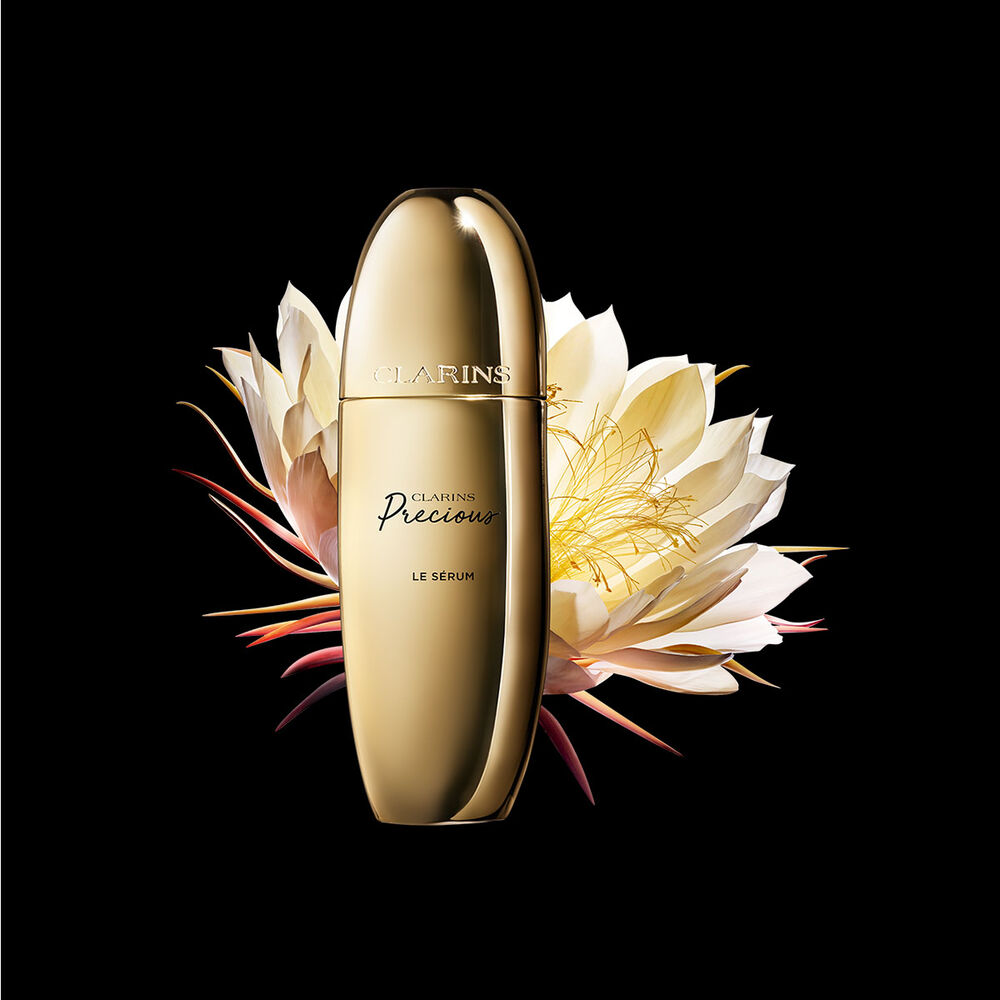 Packshot di Le Serum Clarins Precious vicina a un fiore di Regina della notte su uno sfondo scuro.