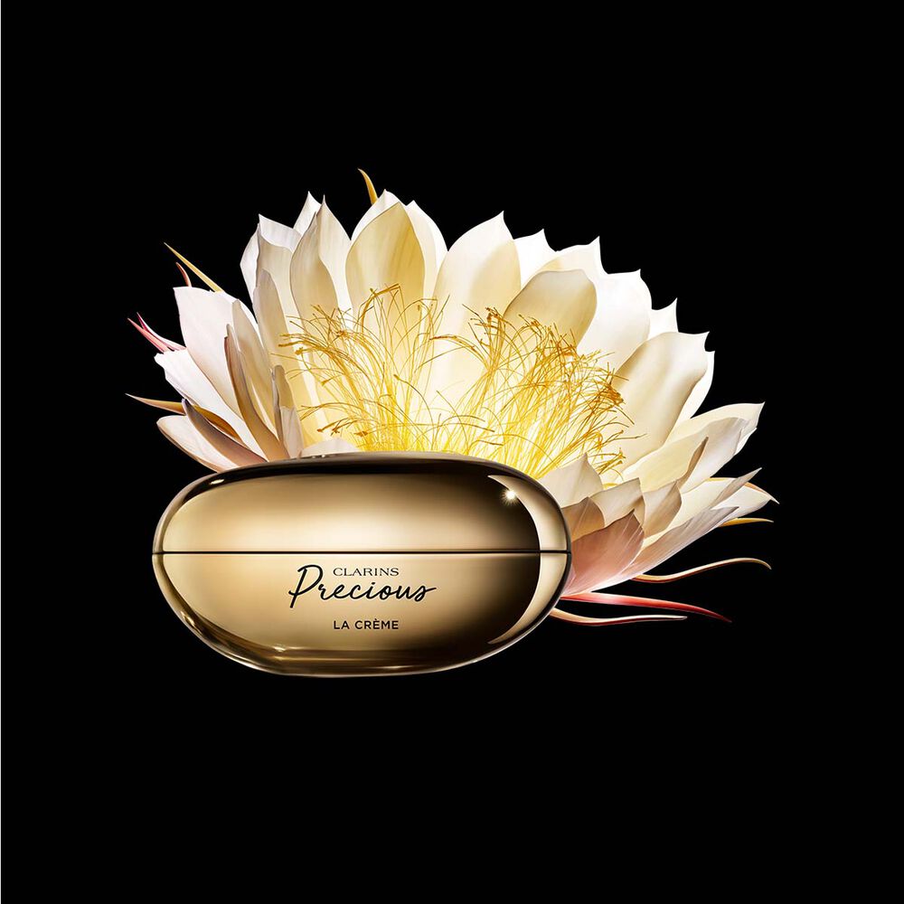 Packshot di La Crème Clarins Precious vicina a un fiore di Regina della notte su uno sfondo scuro.