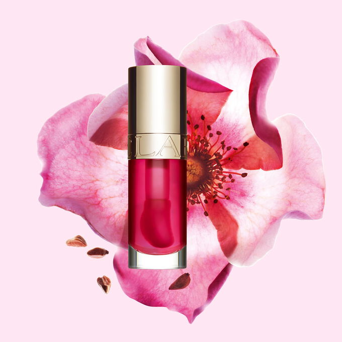 Lip Comfort Oil 04 Pitaya Clarins con benefici skincare davanti a una rosa mosqueta per mettere in risalto gli ingredienti naturali del prodotto.