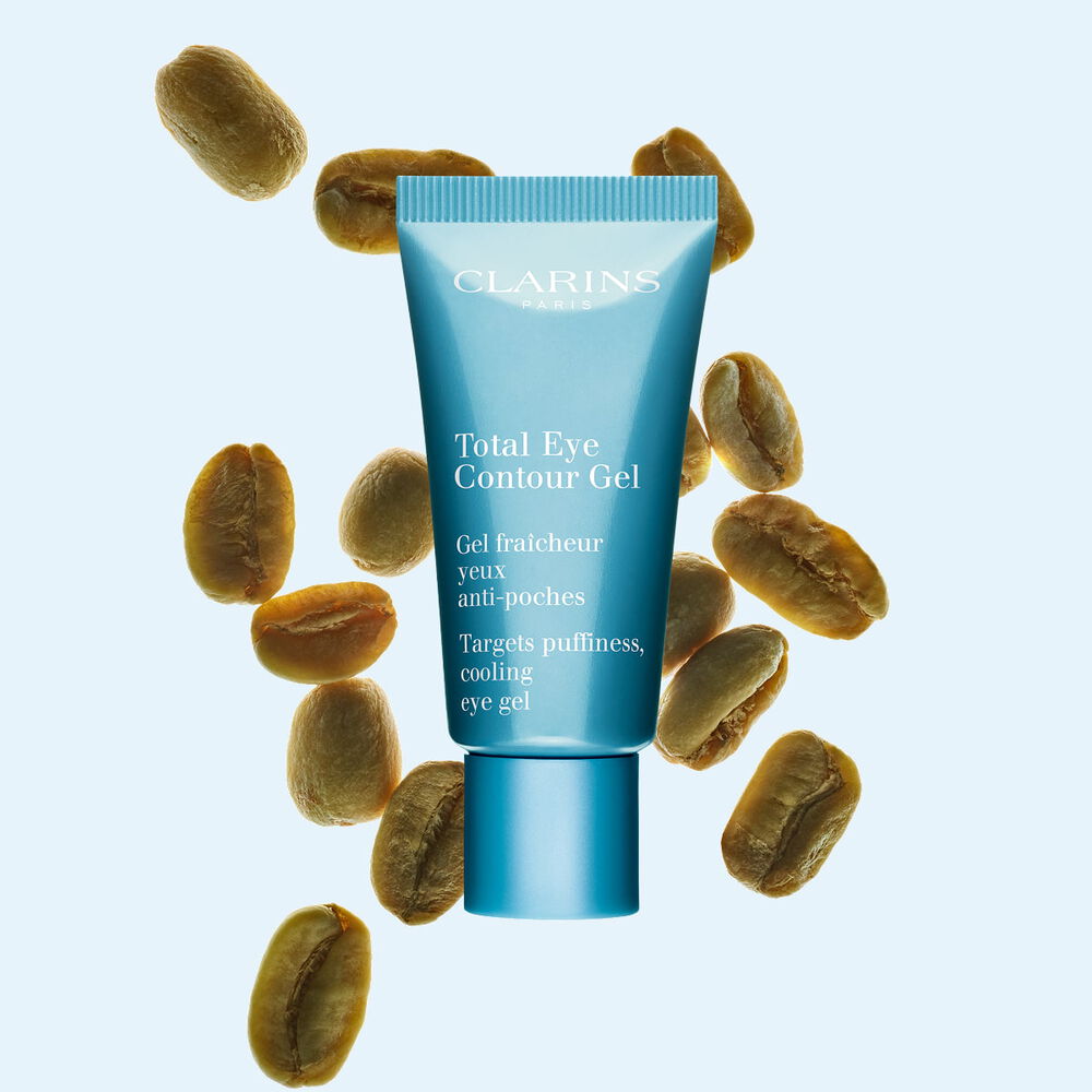 Packshot di un tubetto di Total Eye Contour Gel Clarins vicino a semi di caff&egrave; su uno sfondo blu.