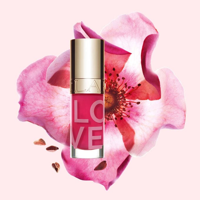 Packshot dell&rsquo;olio labbra della collezione Love in edizione limitata davanti a una rosa su uno sfondo rosa chiaro che mette in risalto il suo colore vivace