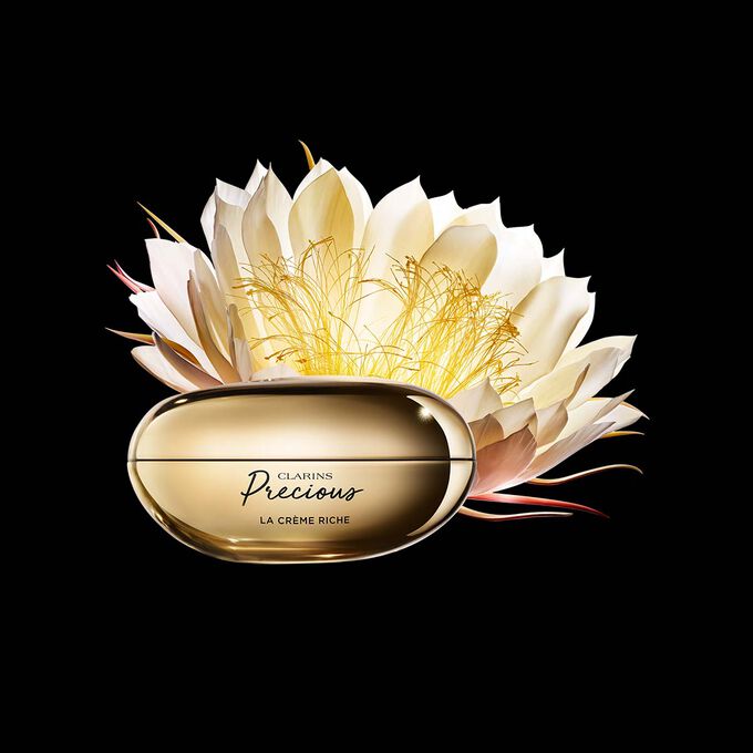 Packshot di La Cr&egrave;me Riche Clarins Precious vicina a un fiore di Regina della notte su uno sfondo scuro.