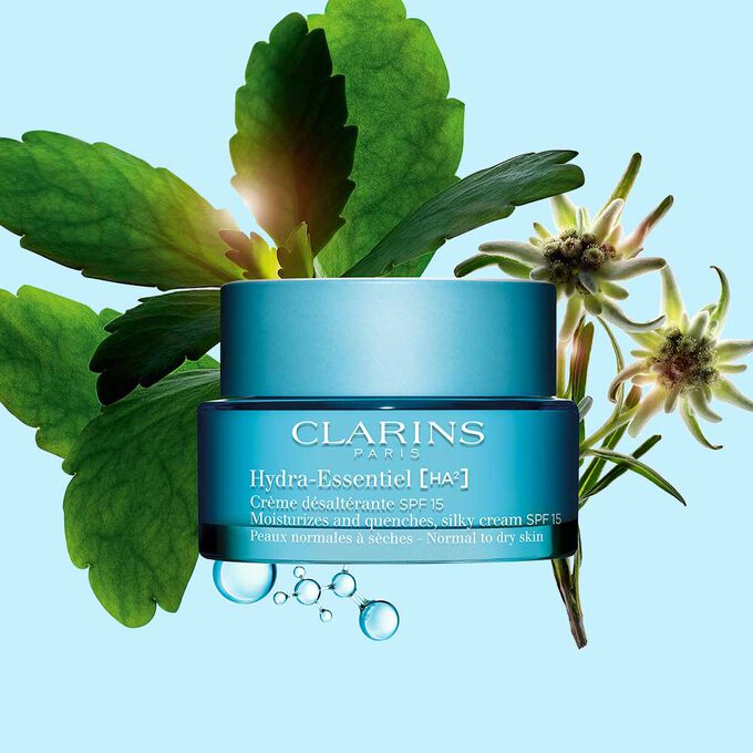 Packshot di Hydra-Essentiel [HA²] Crema SPF15 Clarins accanto ad alcuni fiori di edelweiss su uno sfondo blu.
