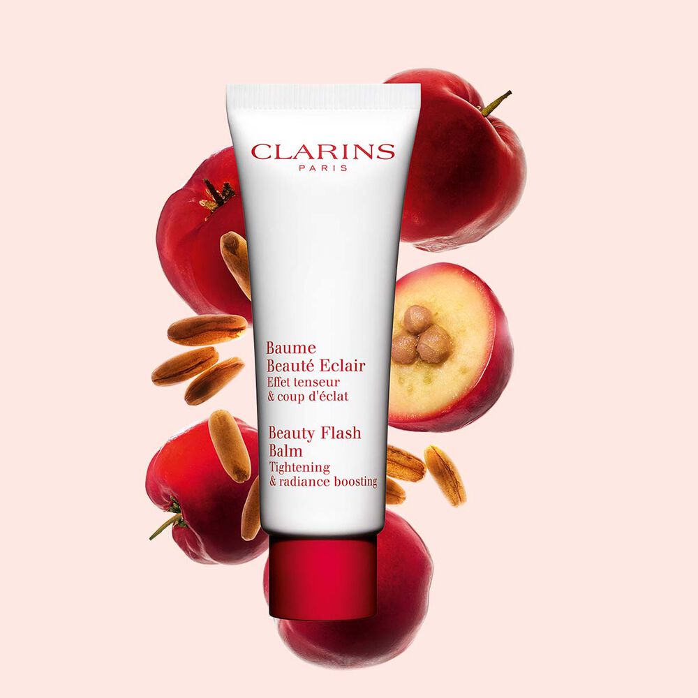 Packshot di un tubetto di Baume Beauté Eclair Clarins vicino a bacche di acerola su uno sfondo color pesca.