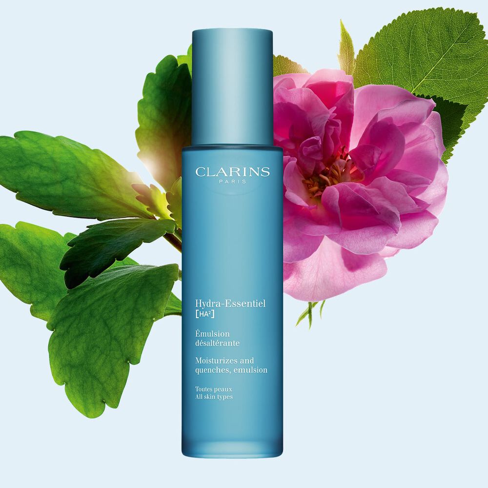 Packshot di Hydra-Essentiel [HA&sup2;] 23 Emulsione Clarins vicina a una rosa di Damasco e a una foglia di pianta di Goethe su uno sfondo blu.