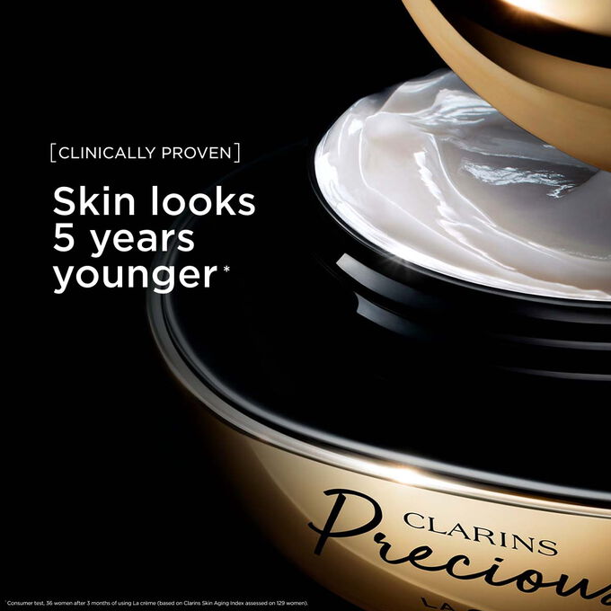 Packshot di La Cr&egrave;me Clarins Precious su uno sfondo scuro, con testo che sottolinea la sua capacit&agrave; di far apparire la pelle 5 anni pi&ugrave; giovane