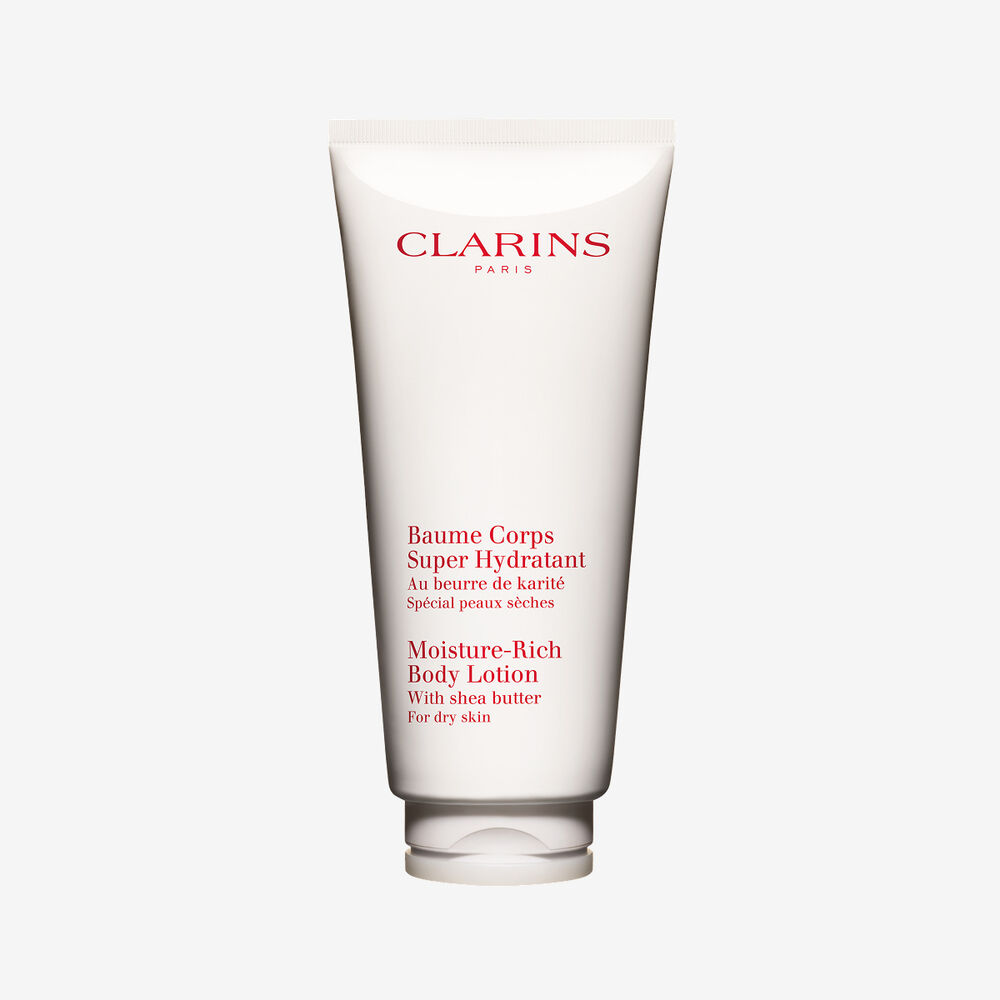 Tubo di Crema Corpo Super Idratante Clarins esposto insieme a gusci di burro di karit&eacute; naturale su un elegante sfondo bianco.