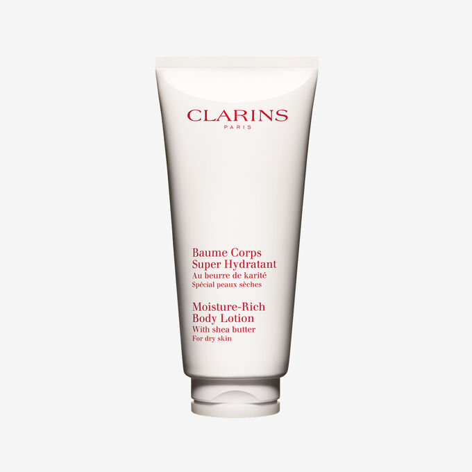 Tubo di Crema Corpo Super Idratante Clarins esposto insieme a gusci di burro di karit&eacute; naturale su un elegante sfondo bianco.