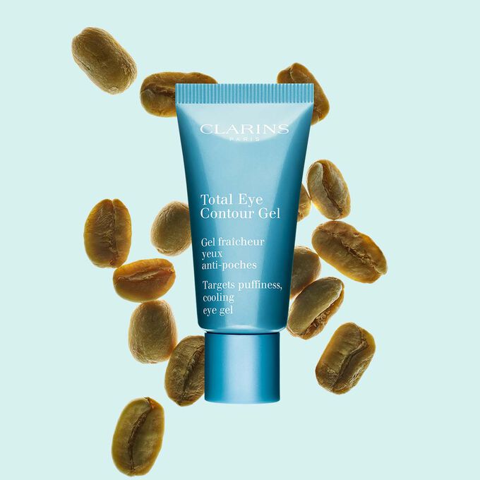Packshot di un tubetto di Total Eye Contour Gel Clarins vicino a semi di caffè su uno sfondo blu.
