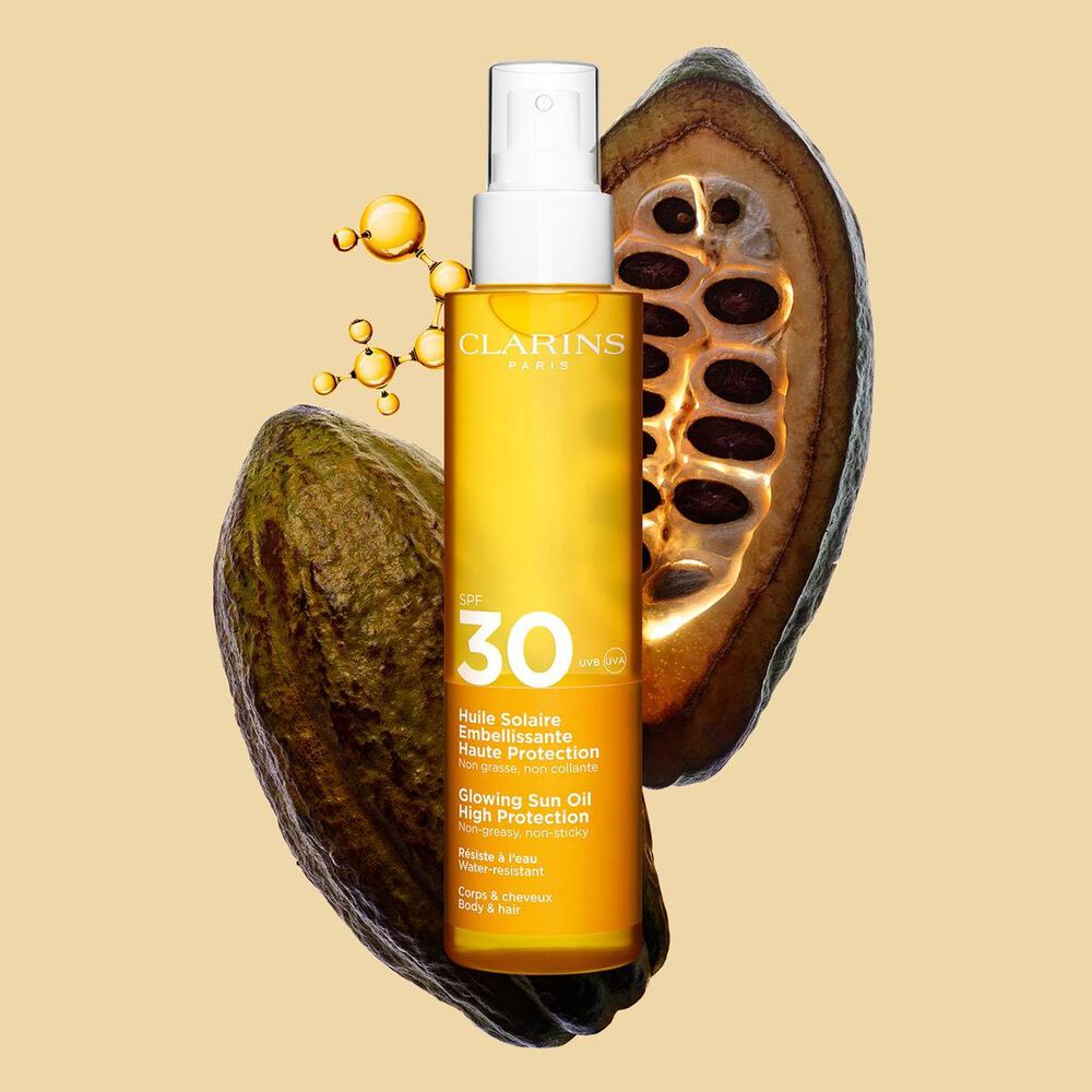 Packshot dello spray arancione di olio corpo e capelli spf 30 vicino a fave di cacao su sfondo arancione chiaro