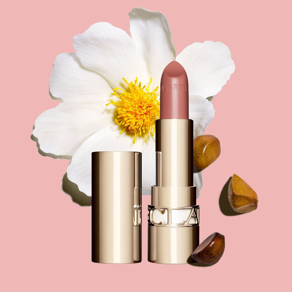 Packshot rossetto Joli Rouge Clarins accanto a un fiore di camelia su sfondo bianco