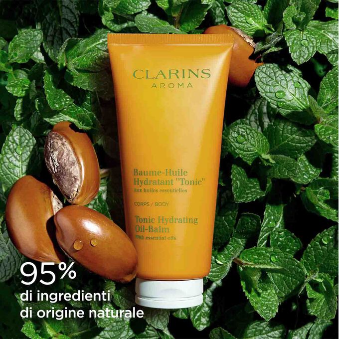 Tubetto di Crema-in olio idratante corpo “Tonicità” Clarins tra foglie di menta e semi di karité per illustrare l’origine naturale dei suoi ingredienti