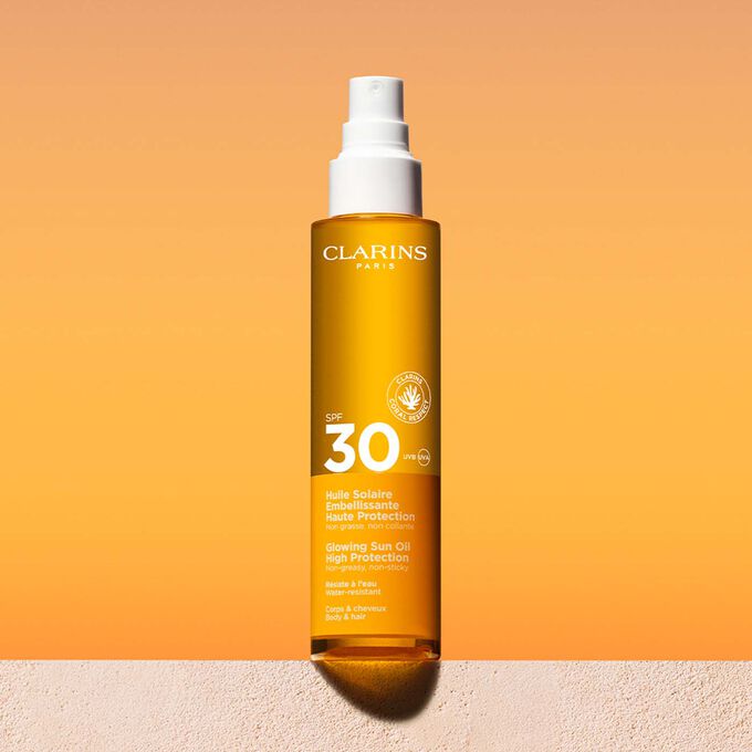 Packshot uno spray di olio solare 30 capelli e corpo con un messaggio che annuncia l’impegno Clarins a tutela dell’ambiente