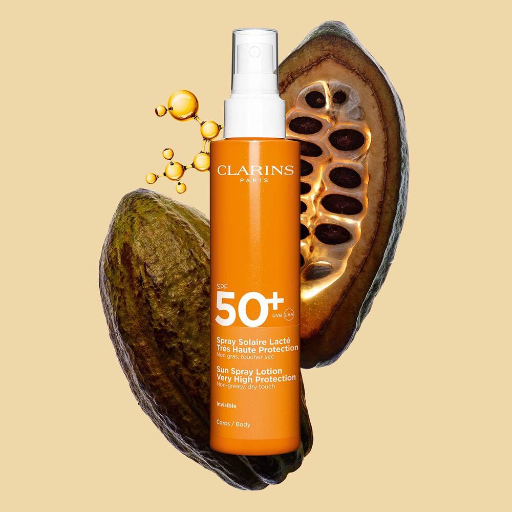 Packshot dello spray arancione scuro di lozione solare corpo spf 50 vicino a fave di cacao su sfondo arancione chiaro